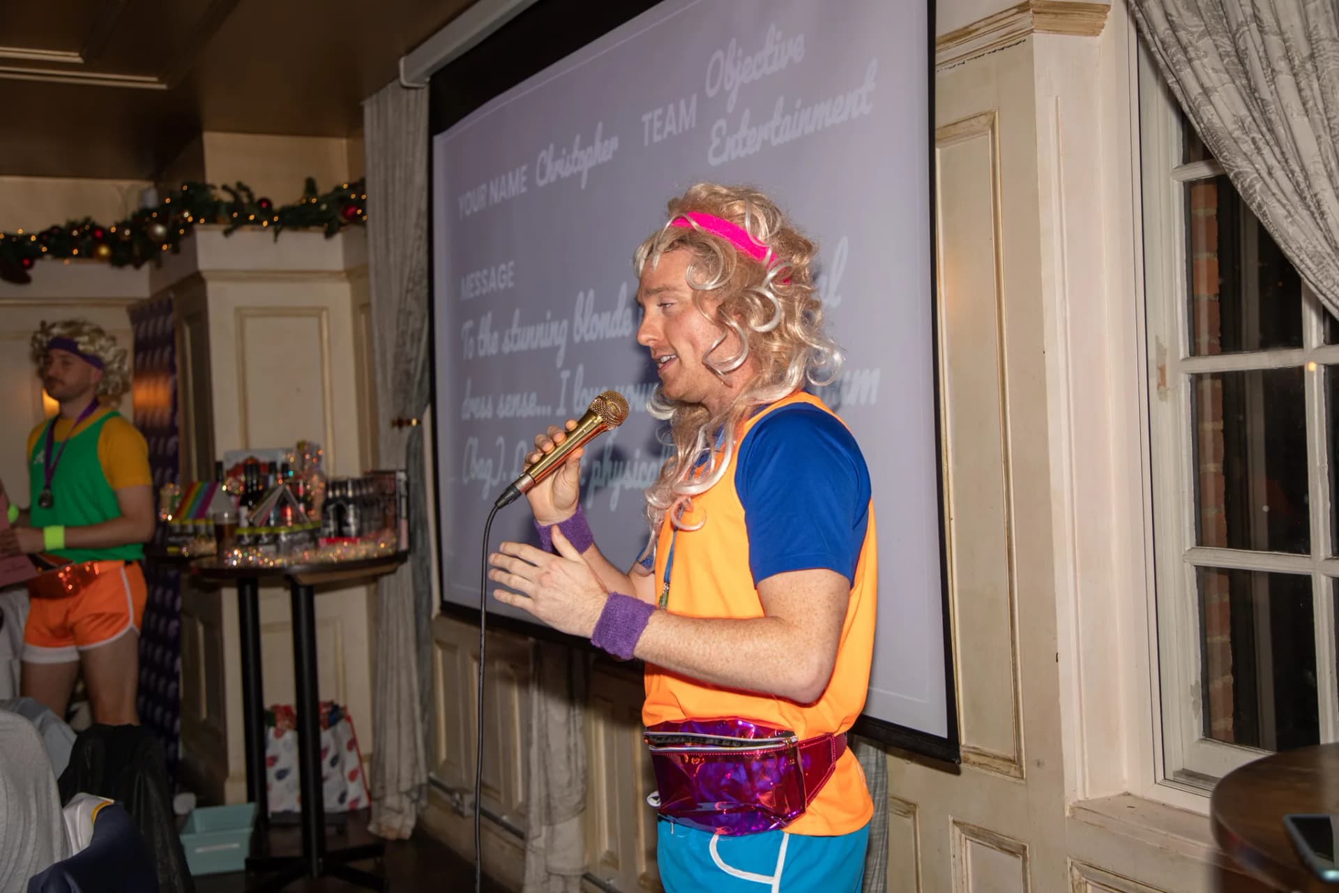 Host in 80s costume at the mic in front of the screen.