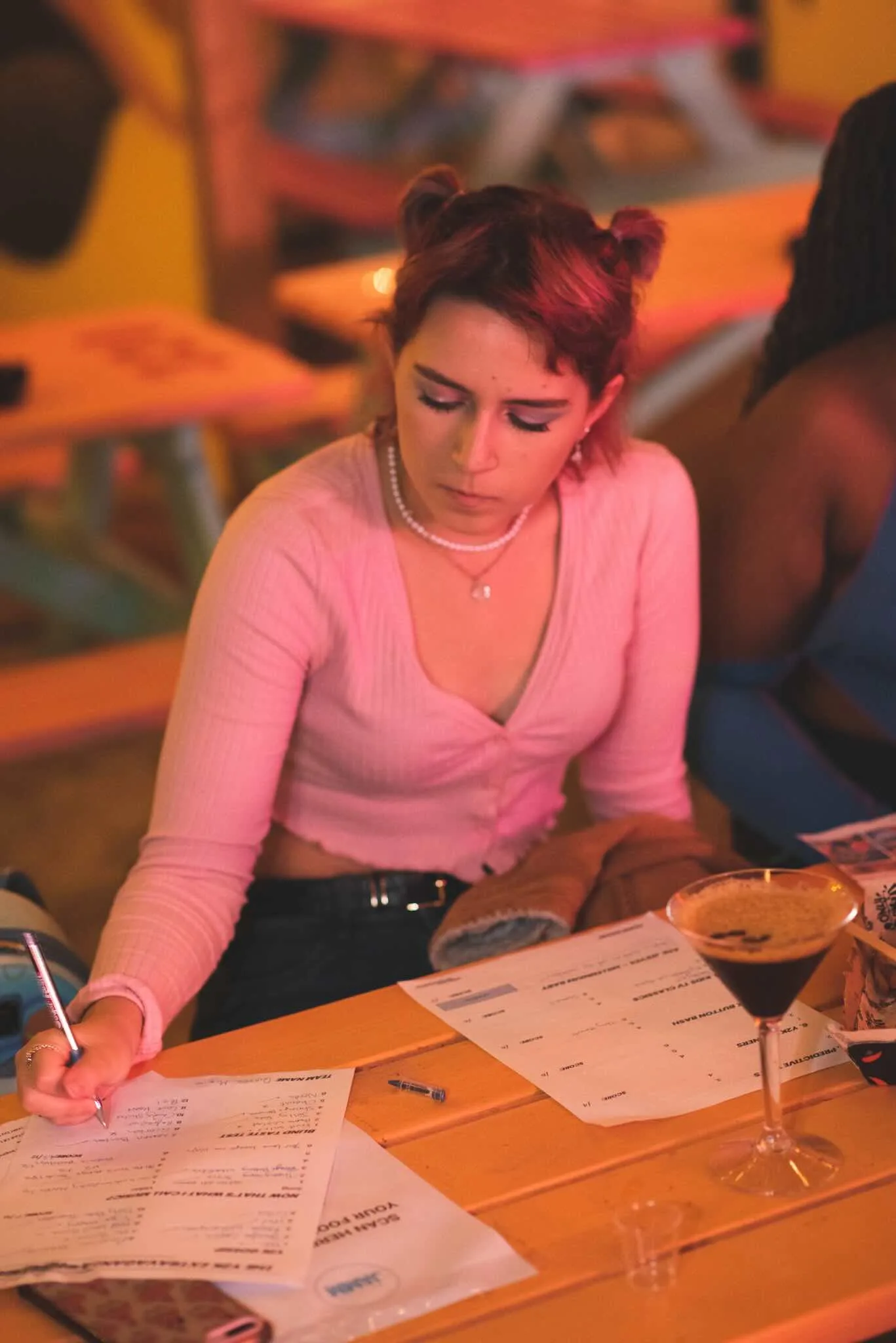 Guest writing answers with a cocktail beside her.